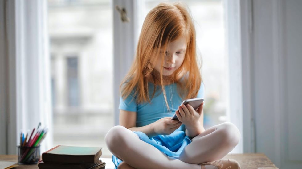 little girl with red hair sitting and looking at a phone