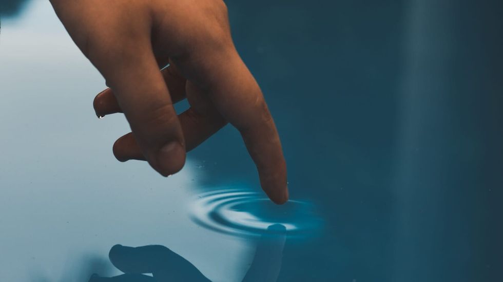 person's hand making a ripple in water