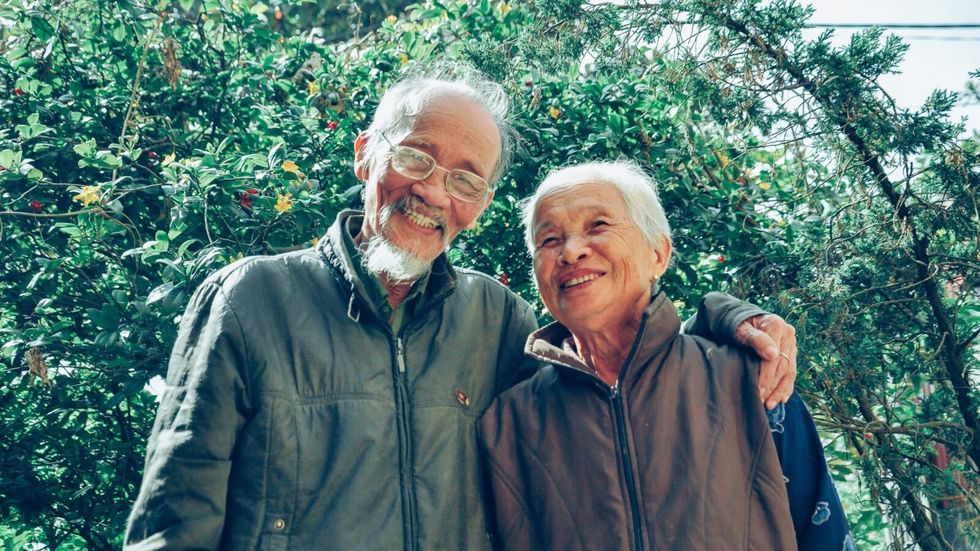 an elderly couple hugging and smiling in front of trees