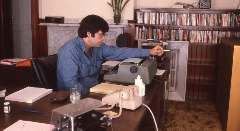 Young Stephen King at his desk writing on his typewriter.