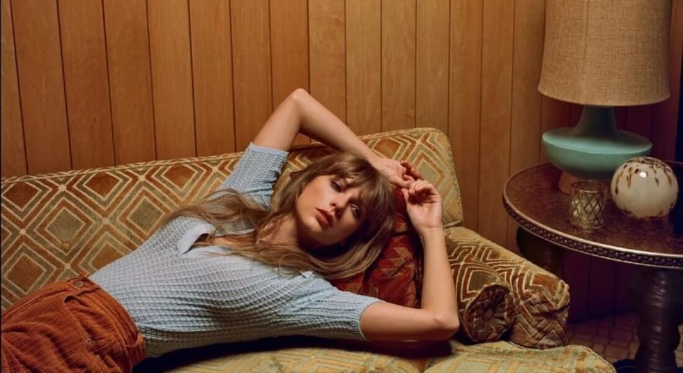Taylor Swift reclining on a couch with her hands above her head new album Midnight