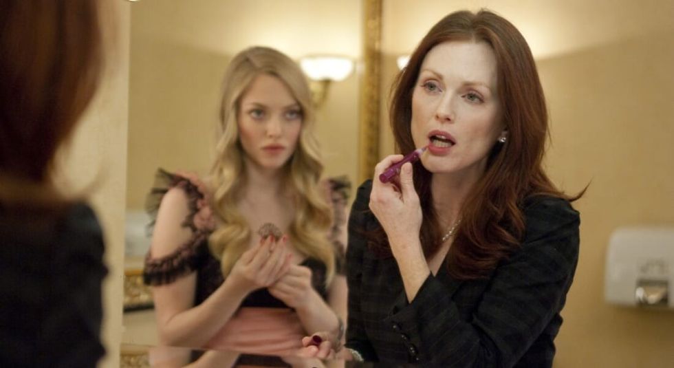 Julianne Moore applying lipstick in the mirror while Amanda Seyfried looks on.