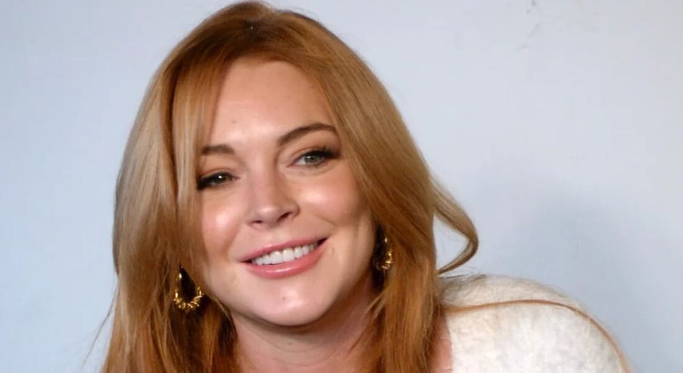 Lindsay Lohan in a white sweater smiling at the camera.