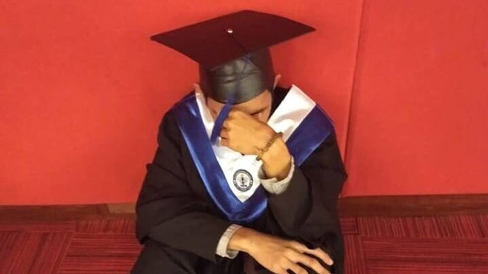 man crying on the floor wearing a graduation cap and gown