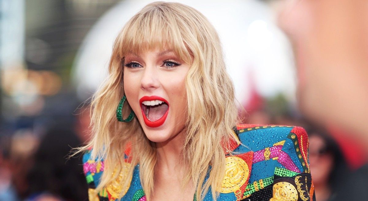 Taylor Swift in a brightly colored jacket screaming in excitement.