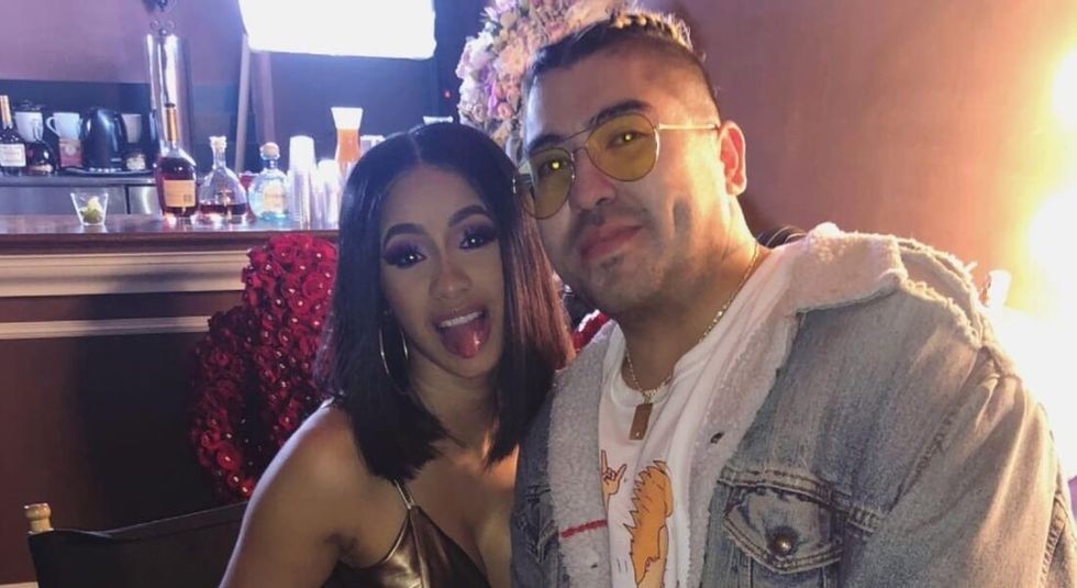 Cardi B in gold bikini, sticking her tongue out at the camera with jewelry designer Isaiah Garza.