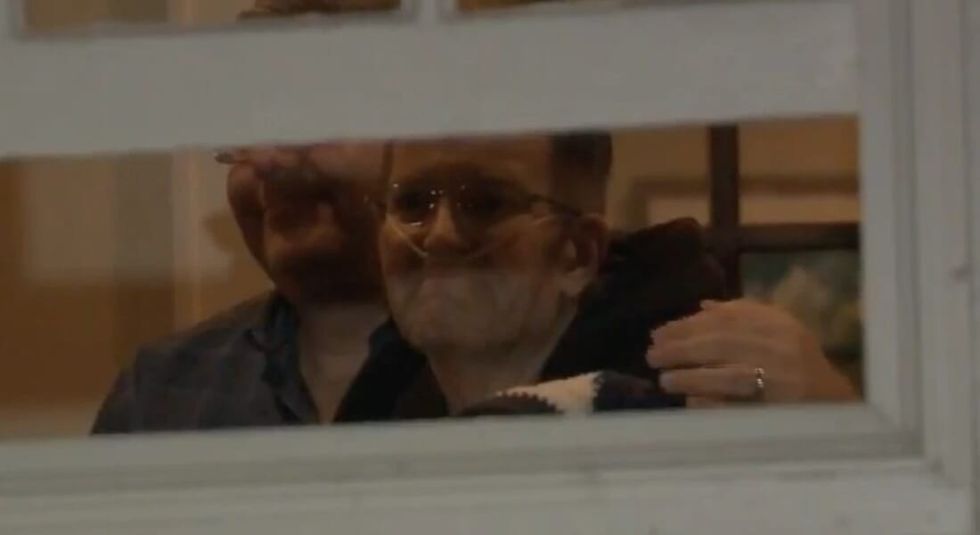 Chris Bradley and husband hugging behind a window.