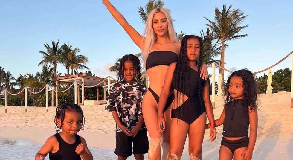 Kim Kardashian and kids posing on a beach in black bathing suits.