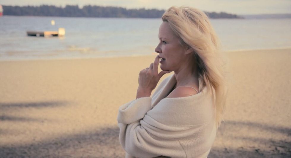 Pamela Anderson in a beige sweater looking at the water. 