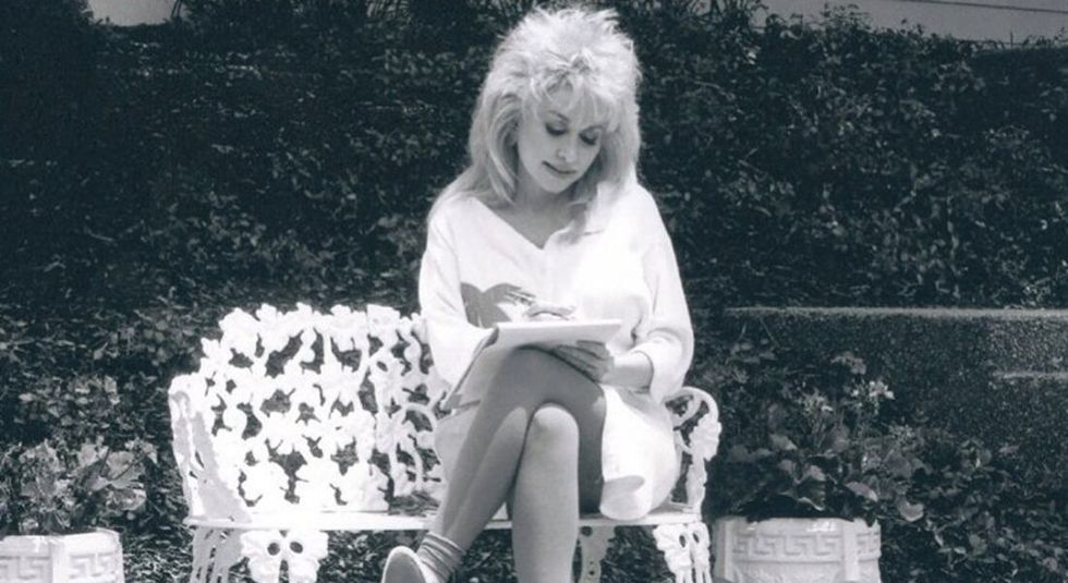 Black and white photo of Dolly Parton writing and sitting on a bench.