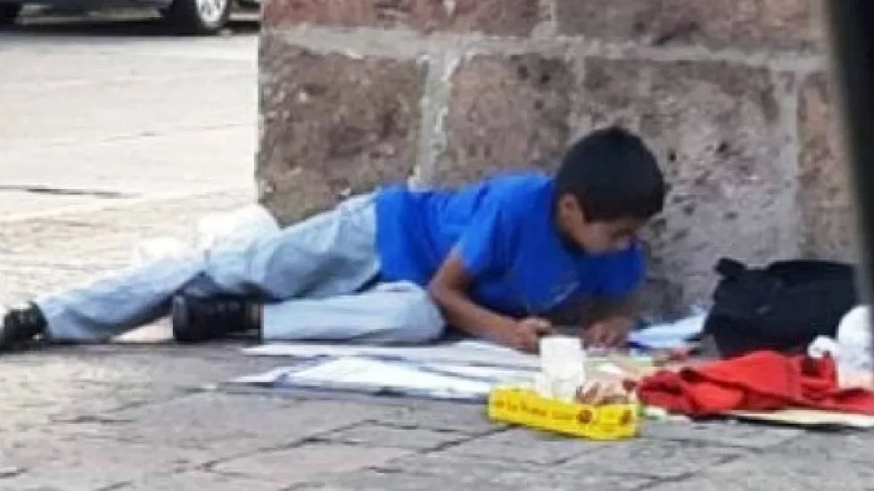 boy in a blue shirt doing homework on the ground