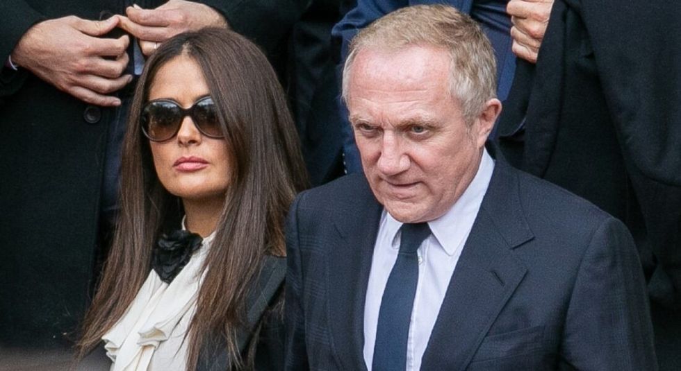 Actress Salma Hayek and husband Francois-Henri Pinault dressed in black suits looking serious.