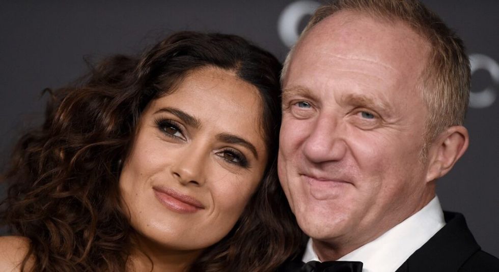 Salma Hayek and Francois-Henri Pinault smiling at the camera while on the red carpet.