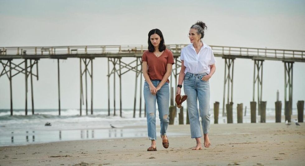 Andie MacDowell walking down a beach with her grey hair up in a bun.