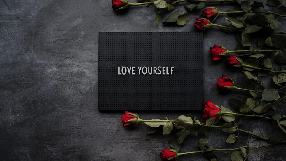 "love yourself" on a black background surrounded by red flowers