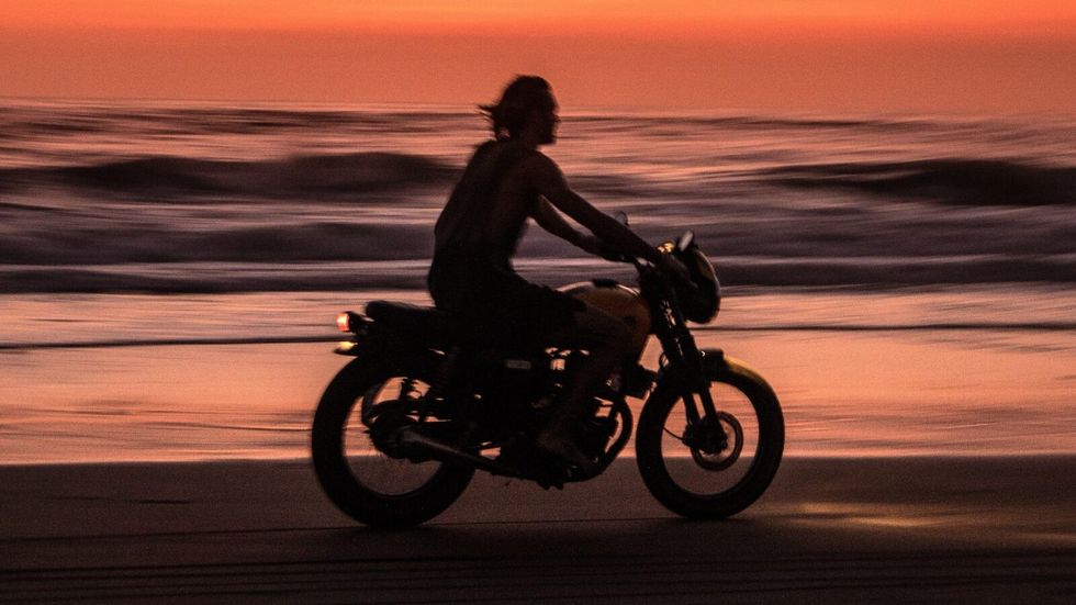 man riding motorcycle on the beach during sunset