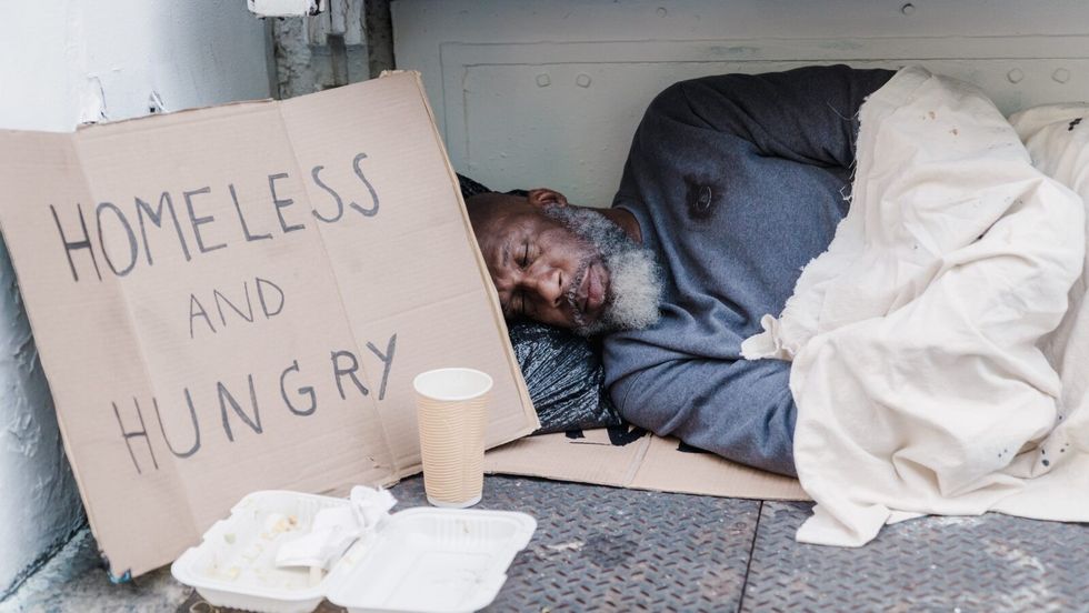 man sleeping on the ground next to a sign reading "homeless and hungry"