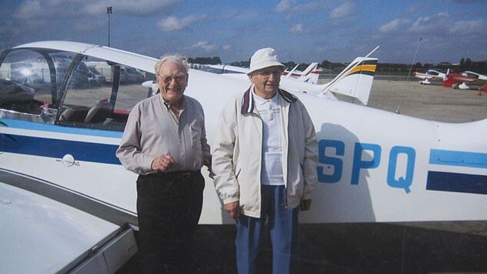 two elderly men standing in front of a plane