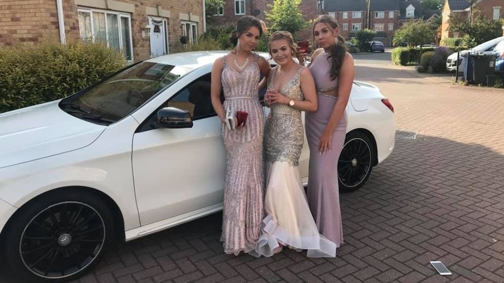 three teen girls wearing prom dresses and standing before a white car