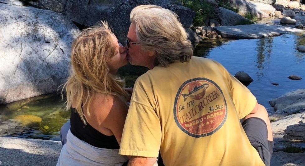 Kurt Russell and Goldie Hawn kissing while sitting on rocks.