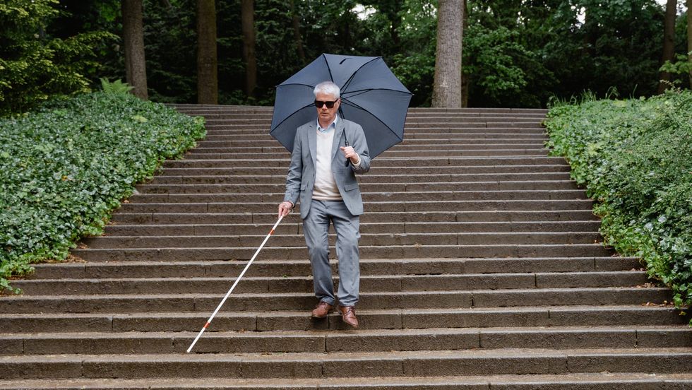 man walking down steps with a walking stick and an umbrella