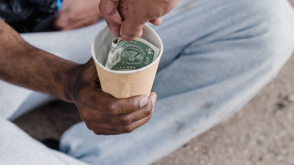 person dropping money into another person's cup