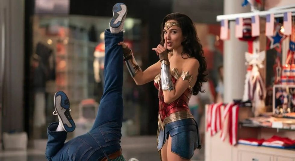 Gal Gadot as Wonder Woman holding a man up by one ankle