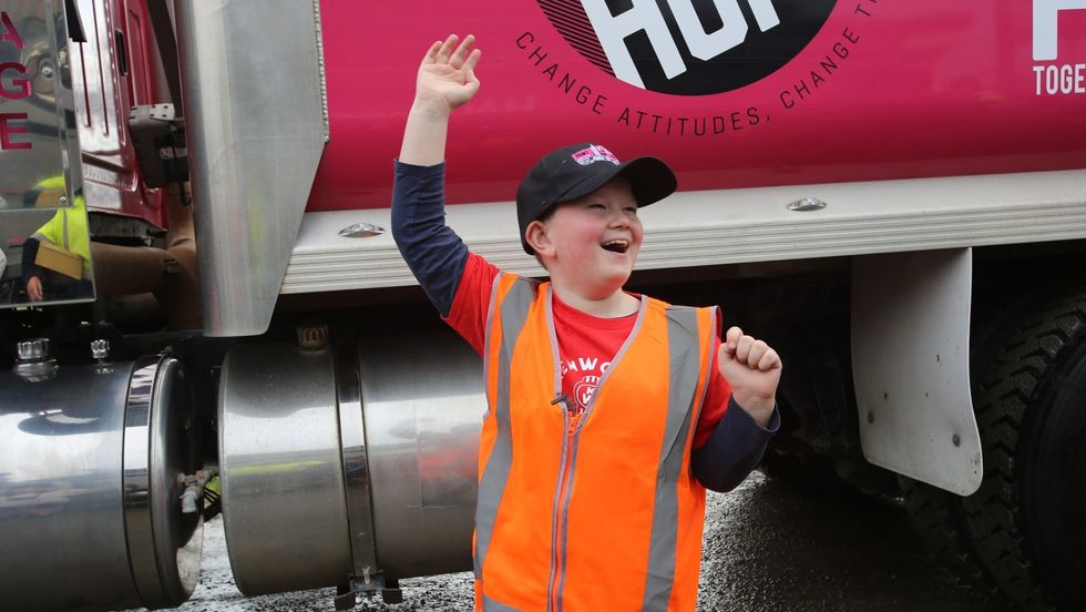 a little boy waving in front of a big rig