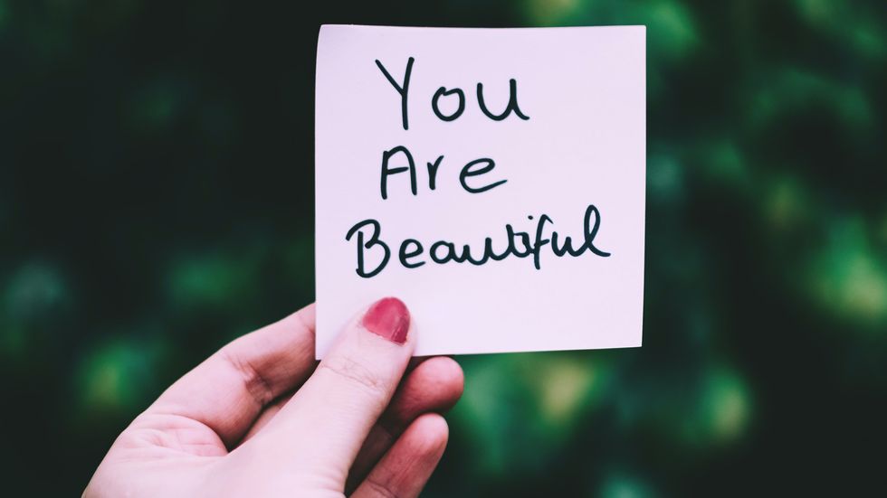woman holding a post-it note with "you are beautiful" written on it