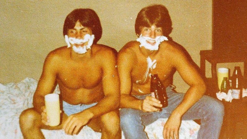 two men sitting on a bed with shaving cream on their faces
