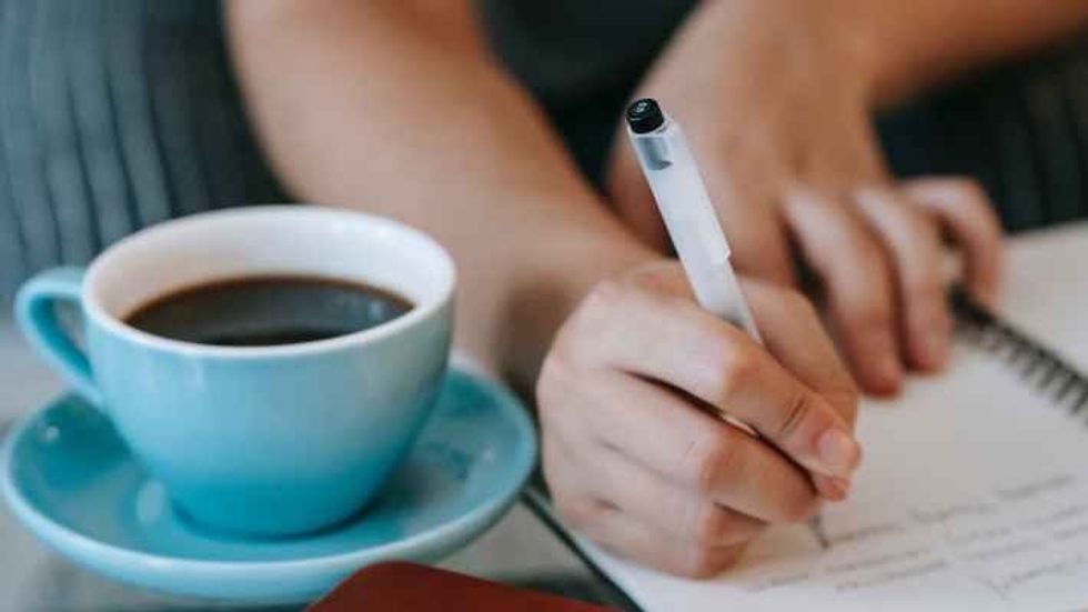 woman writing a note next to a cup of coffee